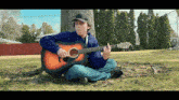 a boy is sitting on the ground playing an acoustic guitar