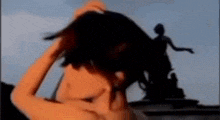 a woman is standing in front of a statue and holding her hair