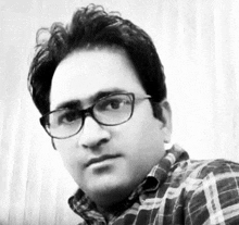 a man wearing glasses and a plaid shirt is taking a picture of himself in a black and white photo .