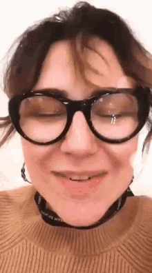 a woman wearing glasses and a brown sweater is smiling .
