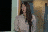 a woman with long hair is smiling while standing in front of a window .