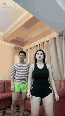 a man and a woman are standing next to each other in a living room . the woman is wearing shorts .