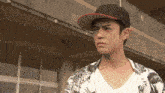 a young man wearing a hat and a floral shirt looks at the camera