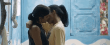 a couple of women kissing in front of a blue wall .