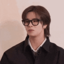 a man wearing glasses and a black jacket is making a funny face .