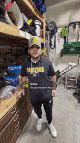 a man wearing a spartans baseball shirt stands in a cluttered garage