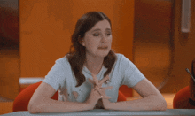 a woman sits at a table with her hands folded