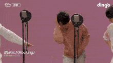 a man in a pink sweater is standing in front of a microphone with a dingo logo on the bottom