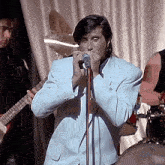 a man singing into a microphone while another man plays a guitar in the background