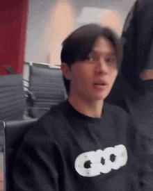 a young man is sitting in a chair wearing a black sweatshirt with the word good on it .