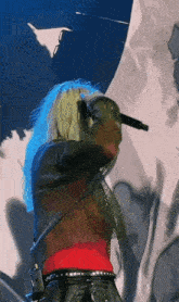 a woman with blue hair singing into a microphone on a stage
