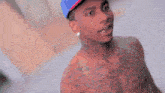 a shirtless man wearing a hat with the letter t on it looks at the camera
