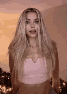 a woman with long blonde hair is wearing a pink crop top .