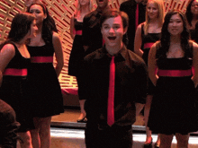 a man wearing a red tie stands in front of a group of women in black dresses