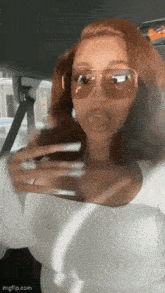 a woman wearing sunglasses and a white top is driving a car .
