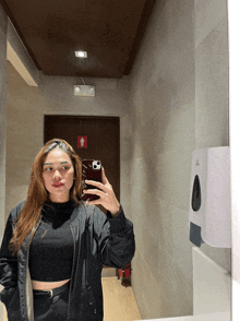a woman in a black jacket takes a selfie in front of a mirror