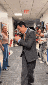 a man in a suit is dancing in a hallway with an exit sign above him