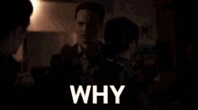 a man in a plaid shirt is talking to another man in a dark room and the word why is on the screen