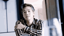 a young man in a striped shirt is sitting in a room with his arms crossed .