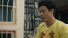 a man wearing a yellow shirt with the letter t on it holds a glass