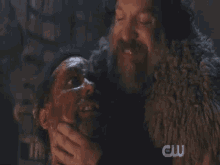 a man holding another man 's face with a cw logo behind him