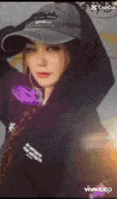 a woman wearing a hat and a hoodie is standing in front of a camera .
