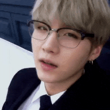 a close up of a young man wearing glasses and a suit and tie .