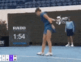 a woman in a blue dress is playing tennis in front of a scoreboard that says 1:54