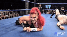 a woman with red hair is laying on the ground in a wrestling ring with a man laying on the ground .