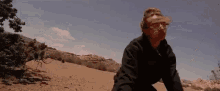 a man wearing glasses is sitting on a sand dune in the desert .