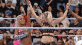 two women in a wrestling ring with their arms in the air and a crowd watching
