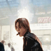 a man in a black leather jacket is standing in front of a sign that says ' welcome '