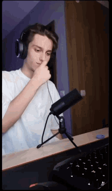 a man wearing headphones is sitting in front of a microphone with his finger on his nose
