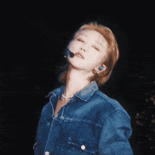 a woman wearing a denim jacket and a microphone looks up