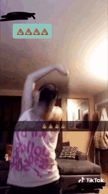 a woman in a pink tank top is dancing in a living room with poop emojis on the screen