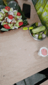 a bowl of vegetables sits on a wooden table next to a cell phone