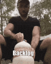 a man in a black shirt is holding a white object with the word backlog written on the bottom