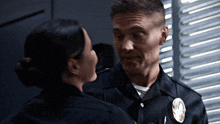 a man and a woman are looking at each other and the man is wearing a badge with the letter t