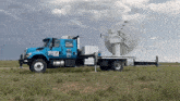 a blue truck with a large antenna on the back is parked on a grassy field