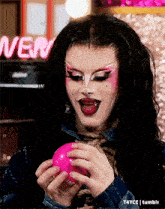 a woman is holding a pink ball in front of a neon sign that says " very "