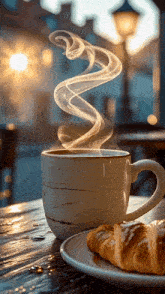 a cup of coffee with steam coming out of it next to a croissant