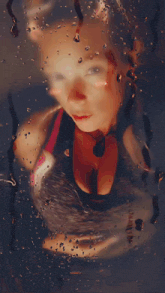 a woman 's face is visible through a window with water drops