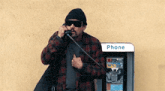 a man is talking on a pay phone next to a phone booth .