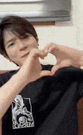 a man wearing a black shirt that says brazem makes a heart shape