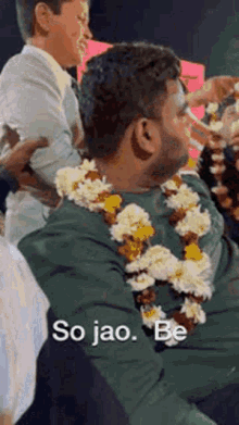 a man wearing a garland of flowers on his neck is sitting in a crowd .