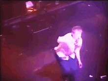 a man is singing into a microphone in a dark room with purple lights
