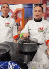 two women wearing floy chef jackets are cooking on a stove