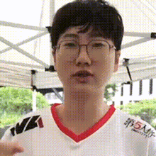 a young man wearing glasses and a white shirt is standing in front of a white tent .