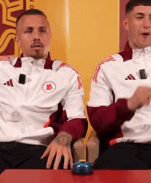a man in a red and white adidas jacket sits next to a man in a white jacket