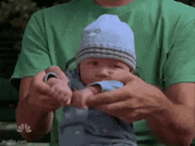 a man is holding a baby in his arms . the baby is wearing a blue hat .